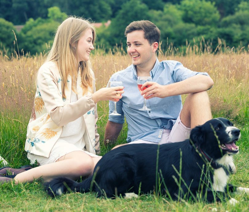 couple enjoying a drink together in a field whilst on holiday with their dog