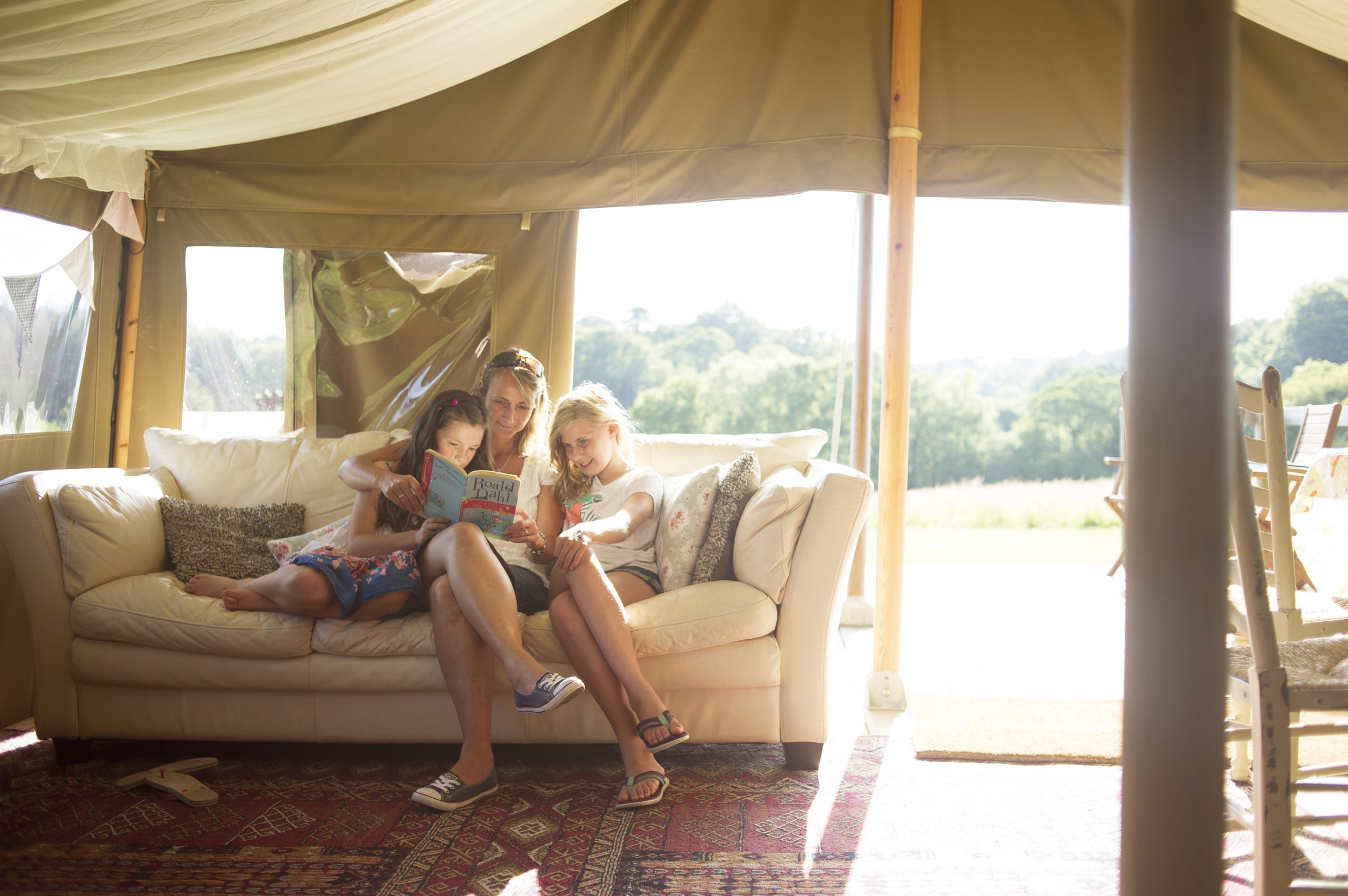 Mother and two girls reading ain a safari ten whilst on a glamping hoilday in Devon UK