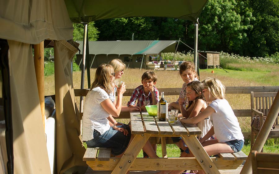 a large family group enjoying an alfresco lunch during a glamping holiday in Devon