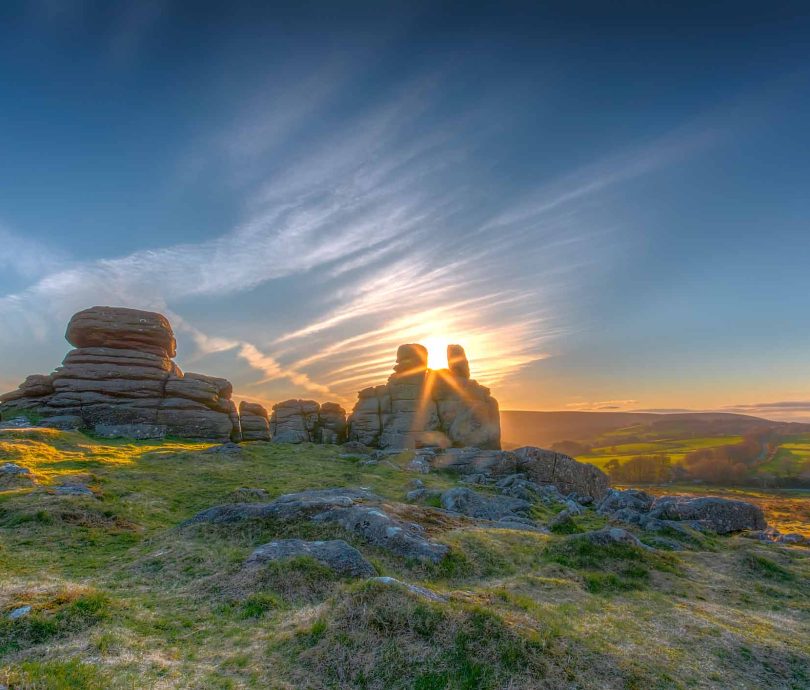 Hound Tor at sunset with the sun shining between the rocks on Dartmoor in Devon