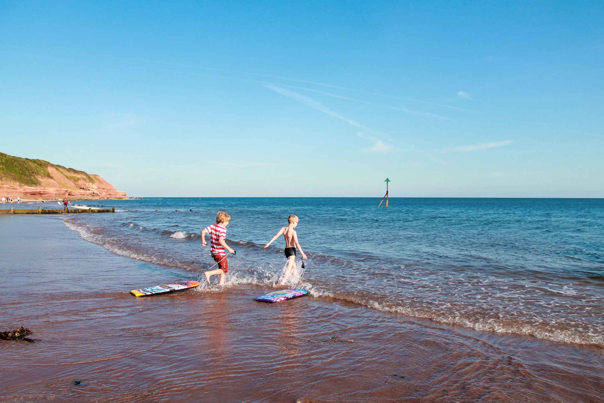 Two boys pulling their body boards into the sea in Devon